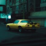 Camaro Z28 - a yellow car driving down a street next to tall buildings